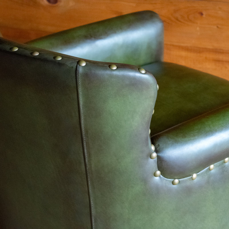 Close-up of the back of a green leather swivel chair against a wooden wall
