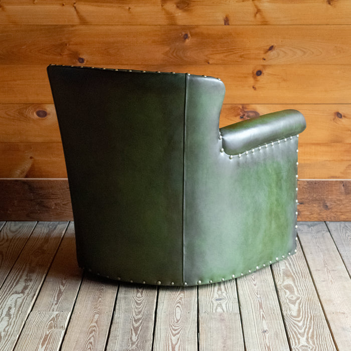 Angled back view of a green leather swivel chair against a wooden wall