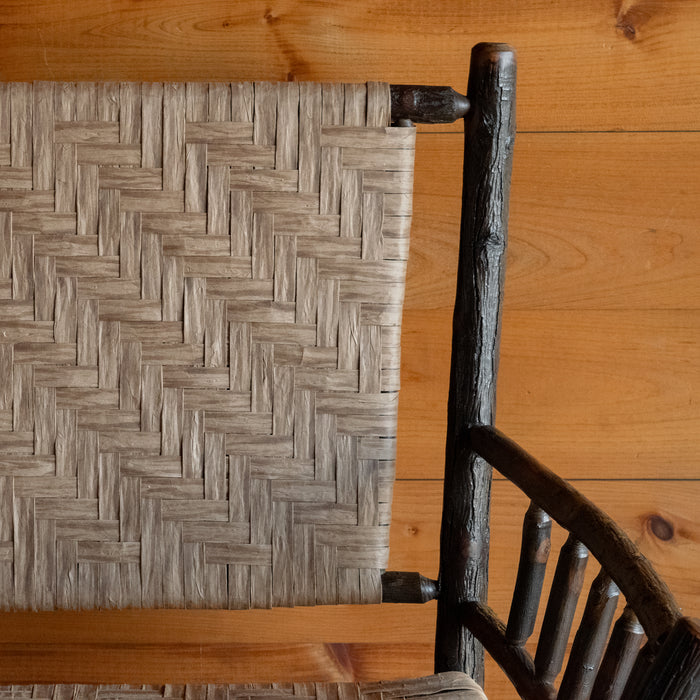 Close-up of the paper splint back of a hickory bench against a rustic wooden wall