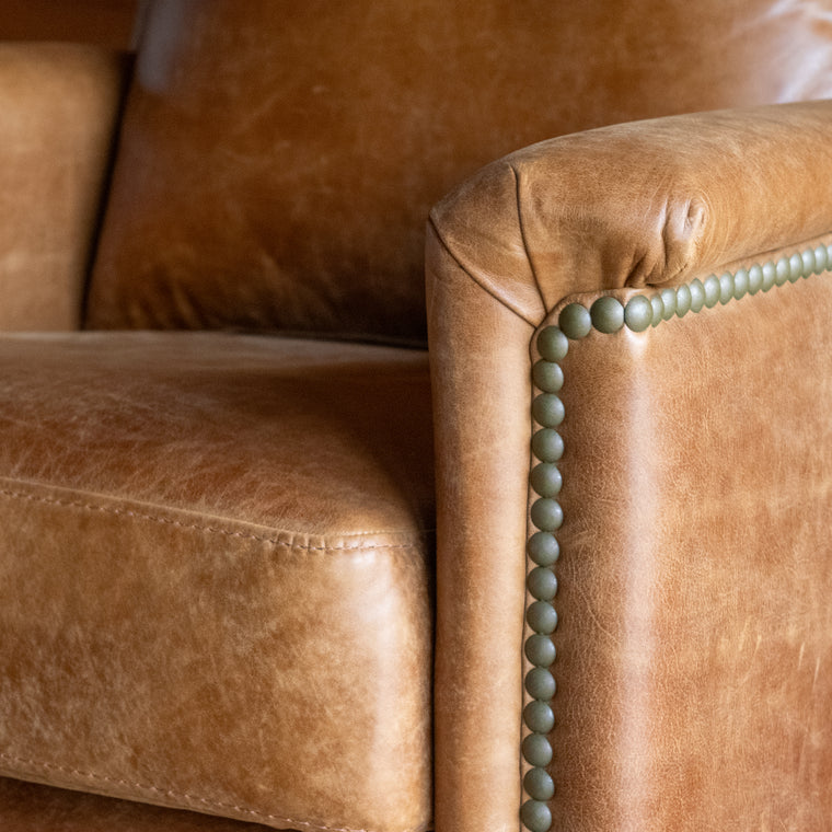 The angled back view of a muted brown leather recliner with nailhead trim against a wooden wall
