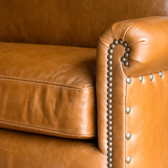 Arm close-up of a full grain leather two-cushion sofa with rolled arms and nailhead trim