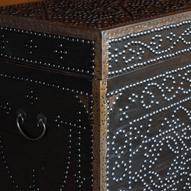 A close-up of the decorative nailheads, metal edge detail, and handle of a dark reclaimed pine storage trunk