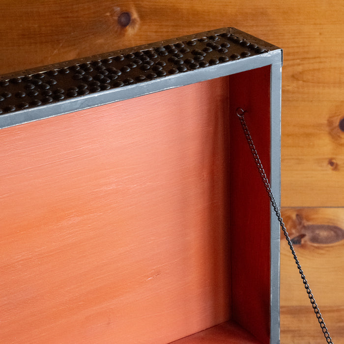 A close-up of the vibrant rust interior of the lid of a dark reclaimed pine storage trunk, decorated with nailheads, against a rustic wooden wall