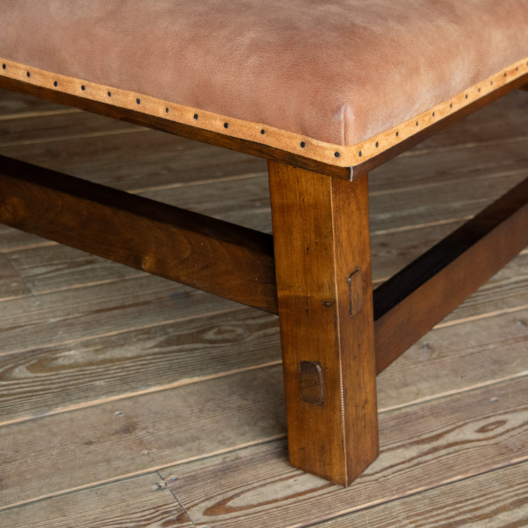 Close-up of the leather upholstery of a rustic leather ottoman with an open hardwood frame on a wide-plank wooden floor