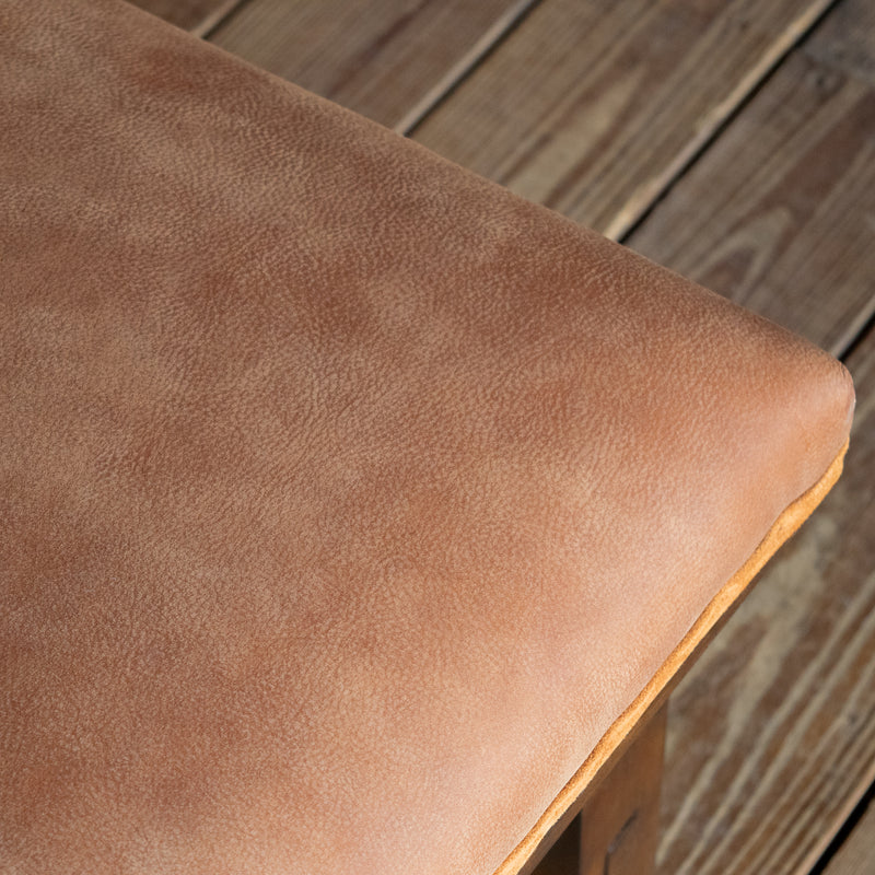 Close-up of the leather upholstery of a rustic leather ottoman with an open hardwood frame on a wide-plank wooden floor