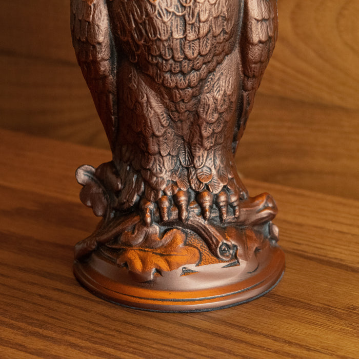 Close-up of the base of a rustic antique old bronze owl-shaped table lamp on a wooden table against a wooden wall