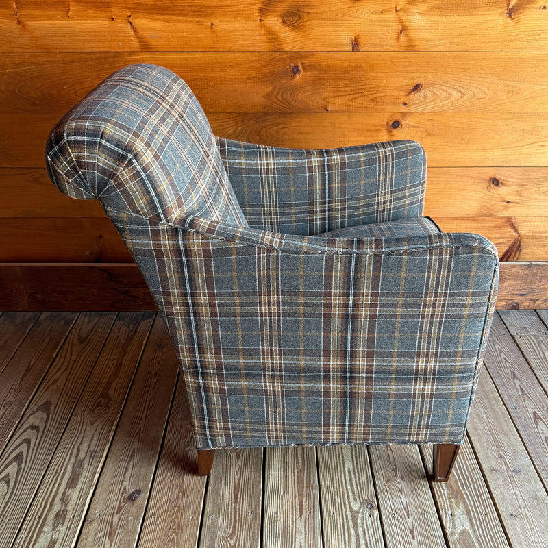 Profile view of a steel blue, gold, and brown plaid armchair against a wooden wall