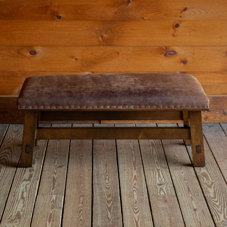 Close-up of the open hardwood frame of an ottoman upholstered in rustic leather on a wide-plank wooden floor