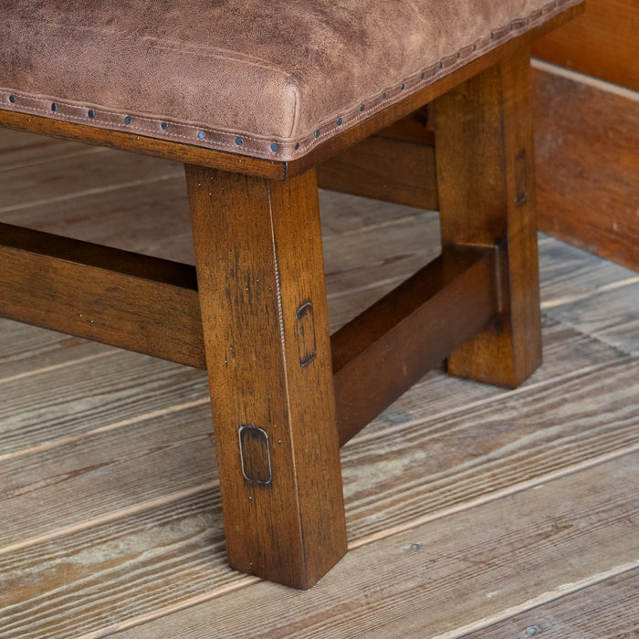 Close-up of the open hardwood frame of an ottoman upholstered in rustic leather on a wide-plank wooden floor