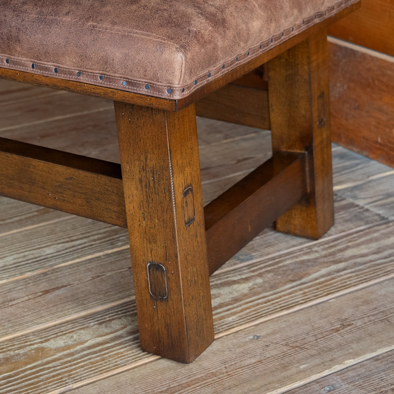 Close-up of the open hardwood frame of an ottoman upholstered in rustic leather on a wide-plank wooden floor