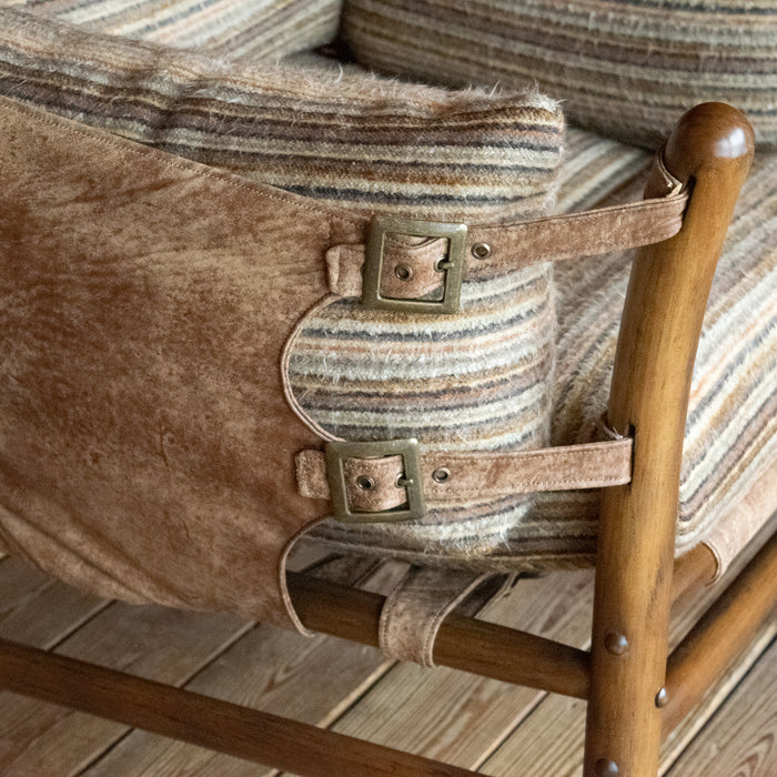 Close-up of the leather side of a safari-inspired chair with striped cushions against a wooden floor