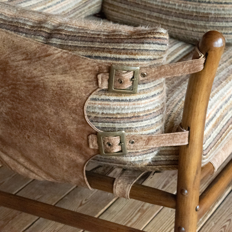 Close-up of the leather side of a safari-inspired chair with striped cushions against a wooden floor