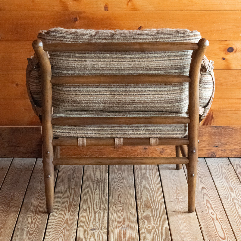 Back view of a safari-inspired chair and ottoman with leather sides and striped cushions on a wooden floor against a wooden wall