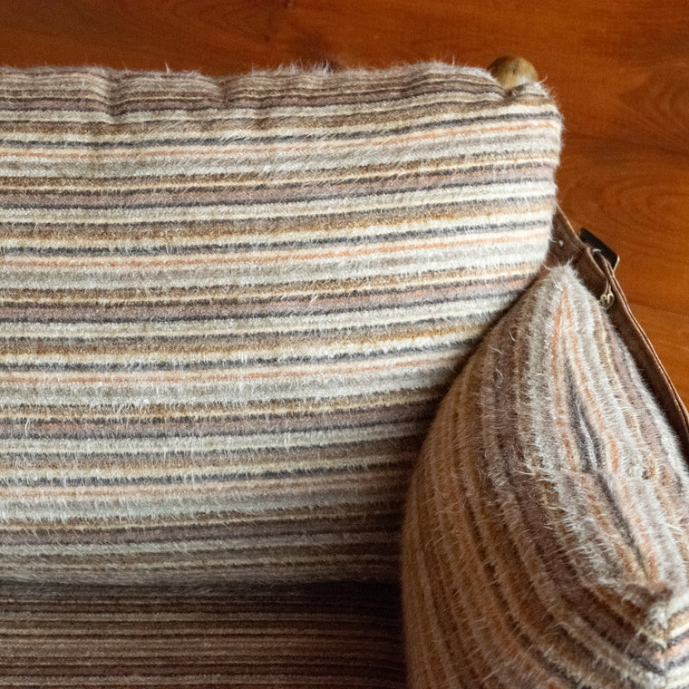 Back view of a safari-inspired chair and ottoman with leather sides and striped cushions on a wooden floor against a wooden wall