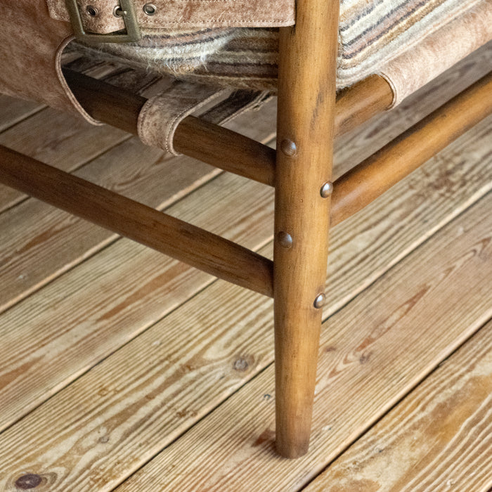Close-up of the leg of a safari-inspired chair with leather sides and striped cushions against a wooden floor