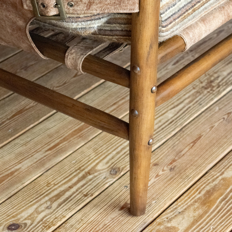 Close-up of the leg of a safari-inspired chair with leather sides and striped cushions against a wooden floor