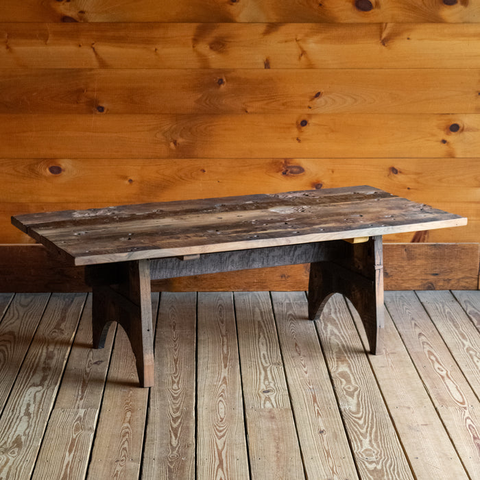 Angled front view of a reclaimed teak wood coffee table on a wide-plank wooden floor against a rustic wooden wall 