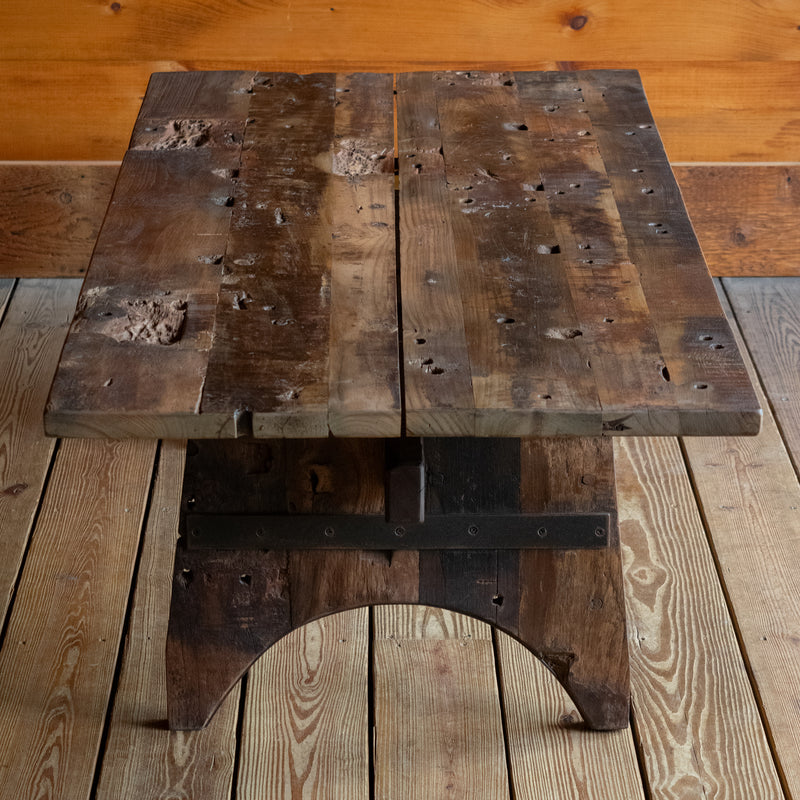 Profile view of a reclaimed teak wood coffee table on a wide-plank wooden floor against a rustic wooden wall 