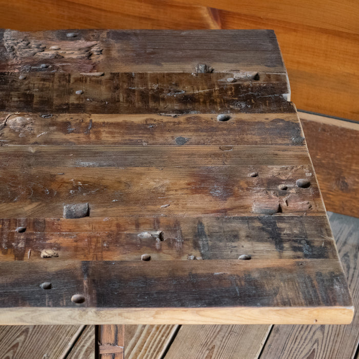 Close-up of the plank-style top of a reclaimed teak wood coffee table against a rustic wooden wall 