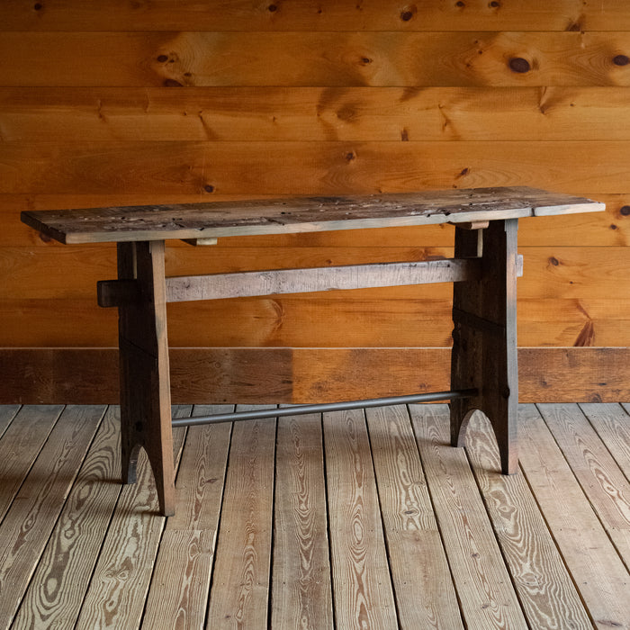 Angled front view of a reclaimed teak wood console table on a wide-plank wooden floor against a rustic wooden wall 
