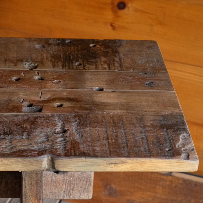 Close-up of the plank-style top of a reclaimed teak wood console table against a rustic wooden wall 