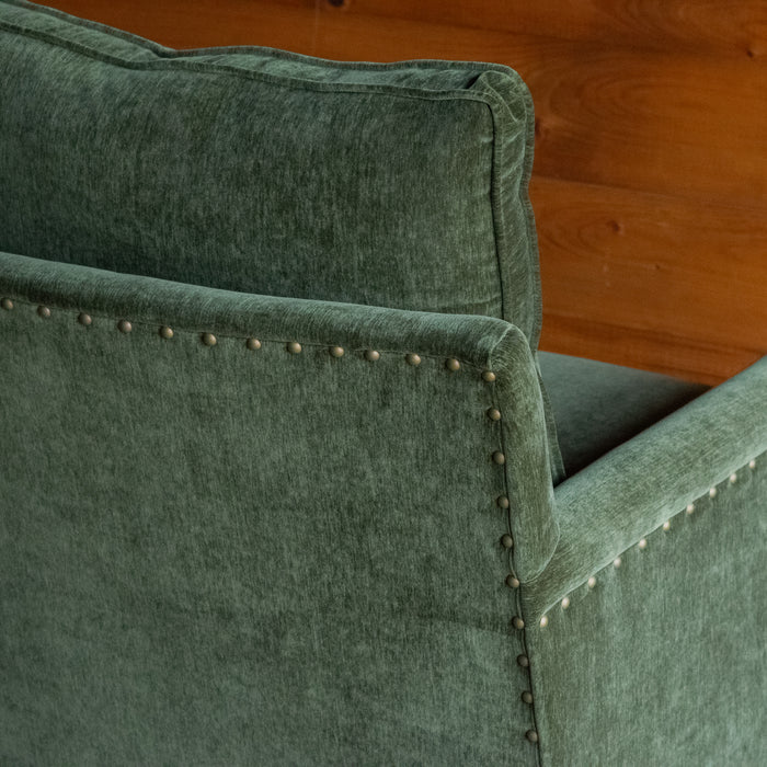 Close-up of the back of a rustic chair with track arms upholstered in a green velvet-chenille fabric against a wooden wall