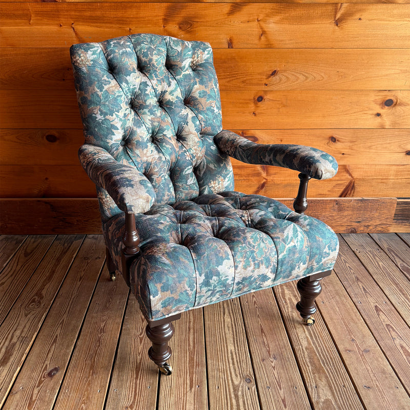 Angled front view of a Victorian-inspired, open arm lounge chair on turned legs against a wooden wall.