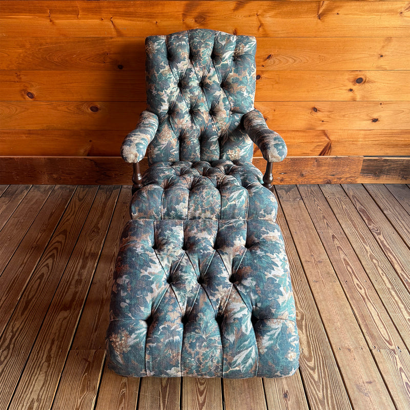 Front view of a Victorian-inspired, open arm lounge chair and ottoman on turned legs against a wooden wall.