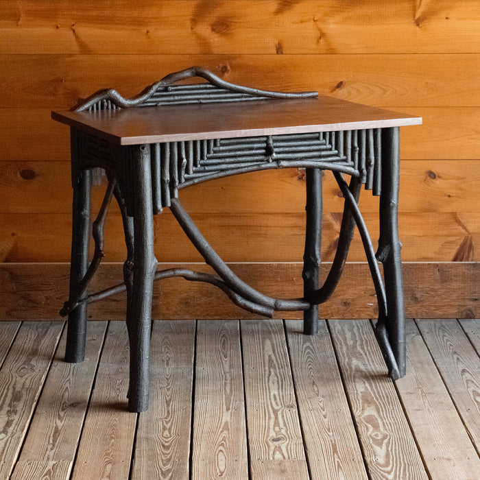 Angled front view of a rustic Adirondack style desk with freeform branches and walnut top against a wooden wall 