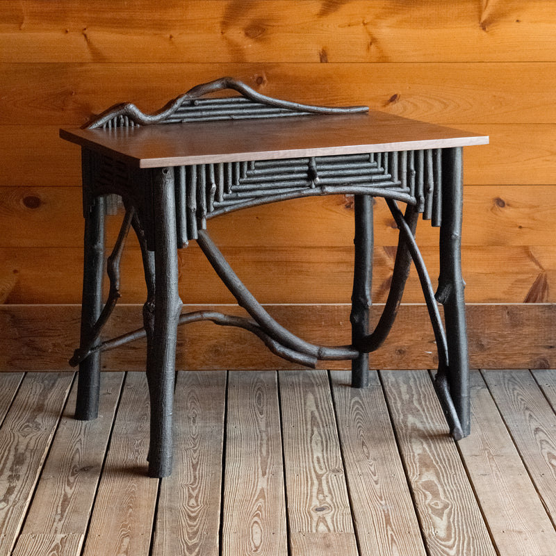 Angled front view of a rustic Adirondack style desk with freeform branches and walnut top against a wooden wall 