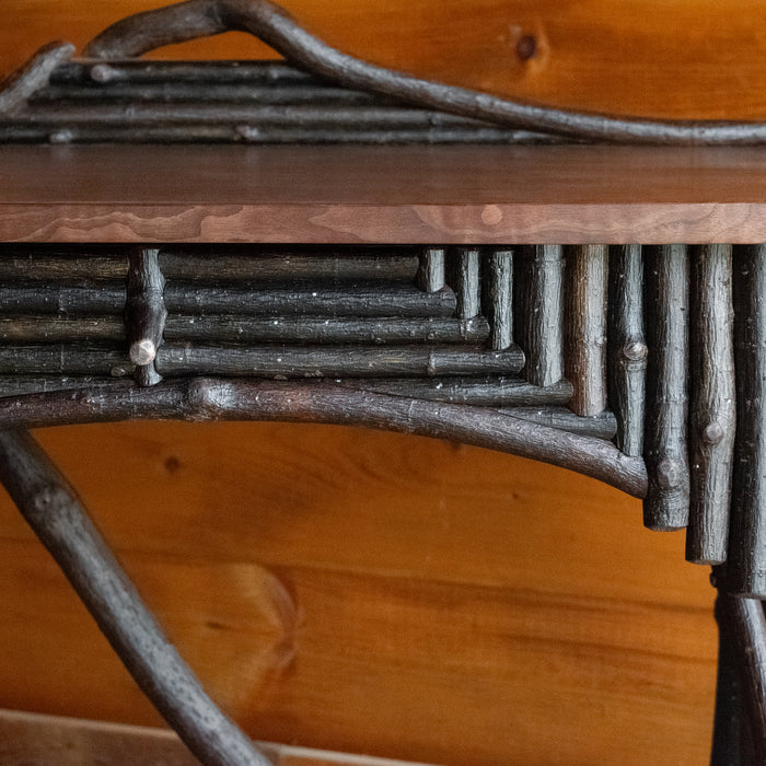 Close-up of the twig work on a rustic Adirondack style desk against a wooden wall 