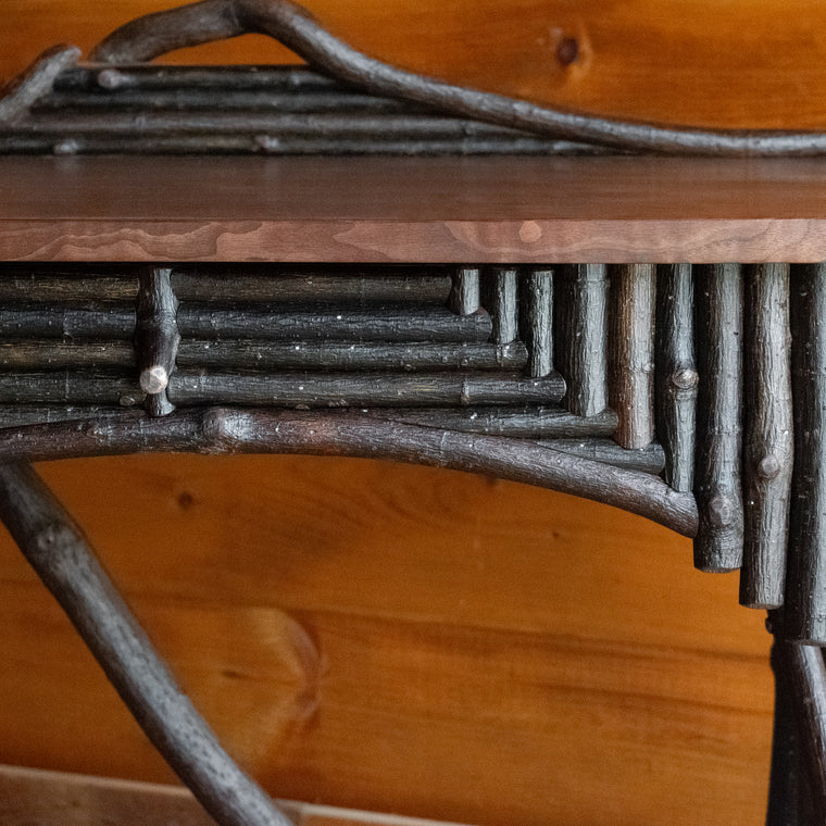 Close-up of the back of a rustic Adirondack style desk with freeform branches and walnut top
