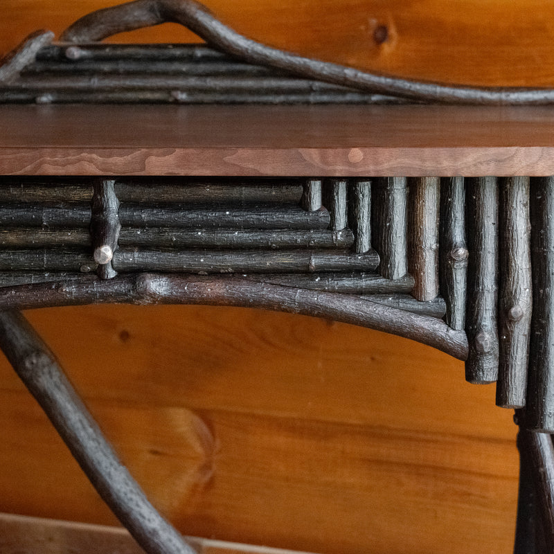 Close-up of the twig work on a rustic Adirondack style desk against a wooden wall 