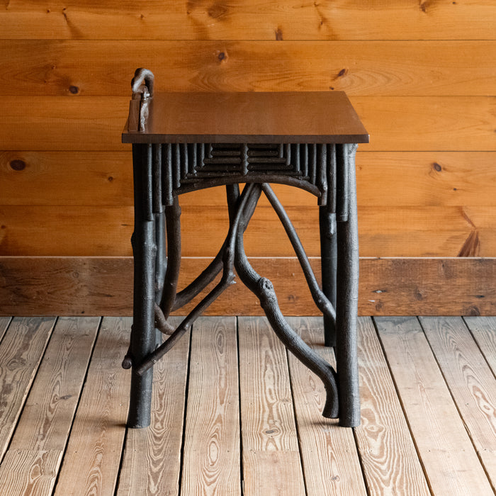Profile view of a rustic Adirondack style desk with freeform branches and walnut top against a wooden wall 