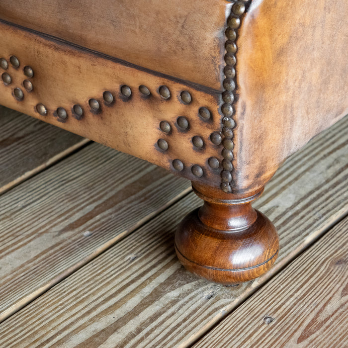 Leg close-up of buffalo leather rolled arm chair with decorative nailhead details