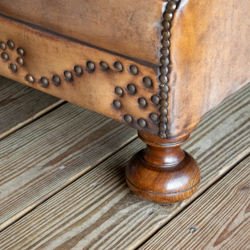 Leg close-up of buffalo leather rolled arm chair with decorative nailhead details
