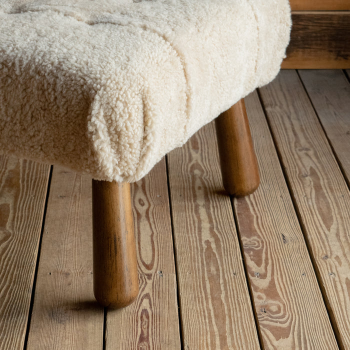 Close-up of the legs of a genuine shearling chaise on a wide-plank wooden floor