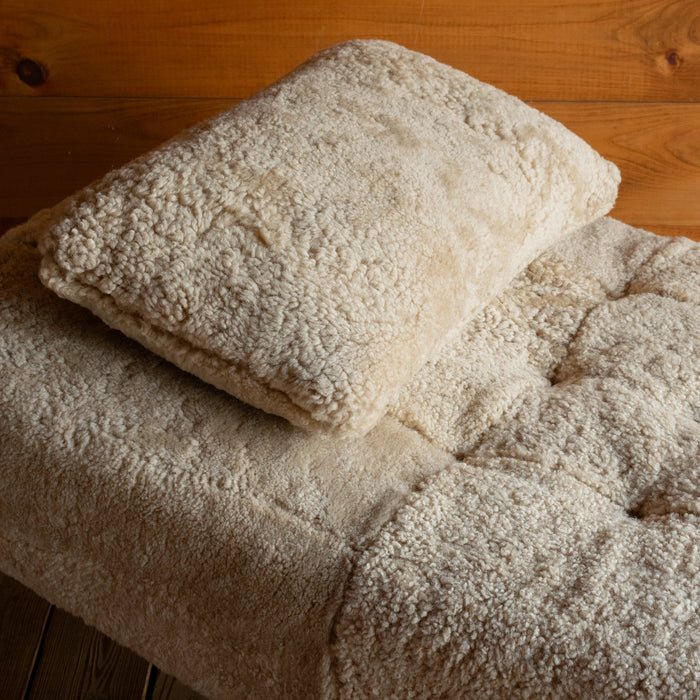 Close-up of the genuine shearling throw pillow on a shearling chaise against a rustic wooden wall