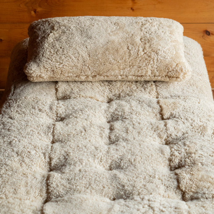 Close-up of the genuine shearling throw pillow and tufting on a shearling chaise against a rustic wooden wall