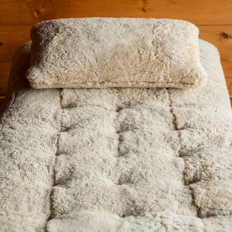 Close-up of the genuine shearling throw pillow and tufting on a shearling chaise against a rustic wooden wall