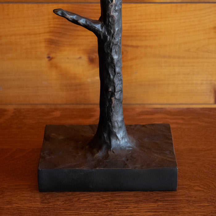 Close-up of the resin tree base of a rustic table lamp on a wooden side table against a rustic wooden wall