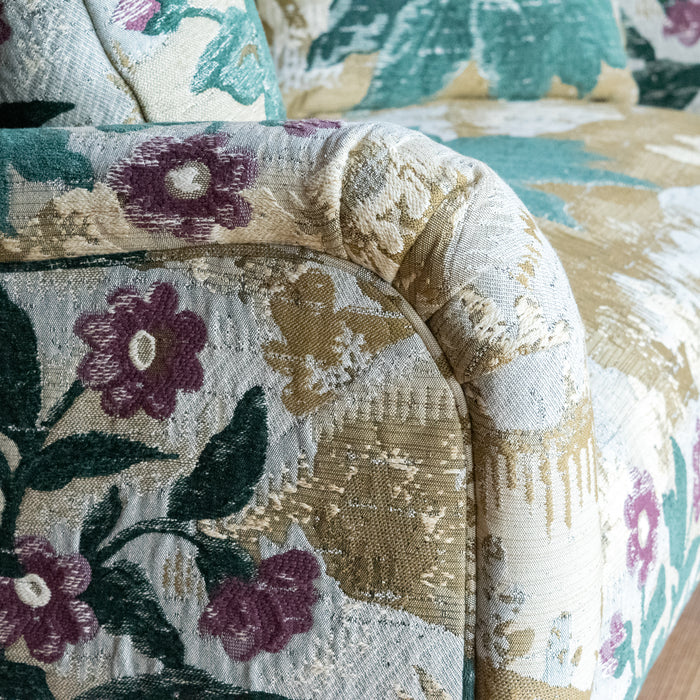 Close-up of the arm of a settee upholstered in a floral fabric with two matching throw pillows