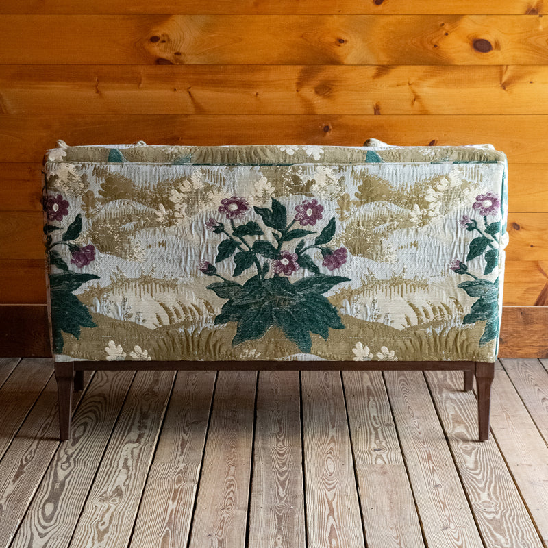 Back view of a settee upholstered in a floral fabric against a wooden wall 