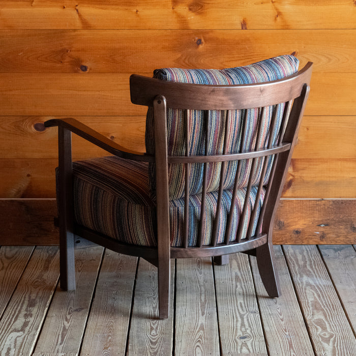 Angled back view of an exposed wood frame chair with striped cushions against a wooden wall