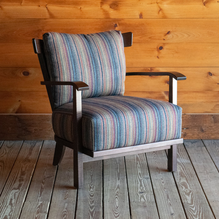 Angled front view of an exposed wood frame chair with striped cushions against a wooden wall