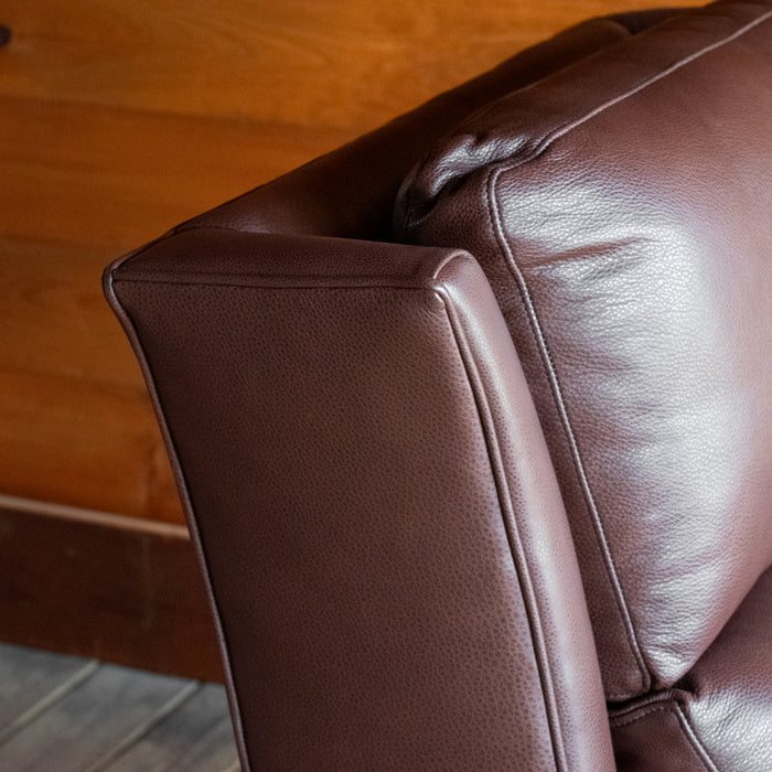 Leather close-up of a dark brown leather recliner with rolled arms and nailhead trim against a wooden wall
