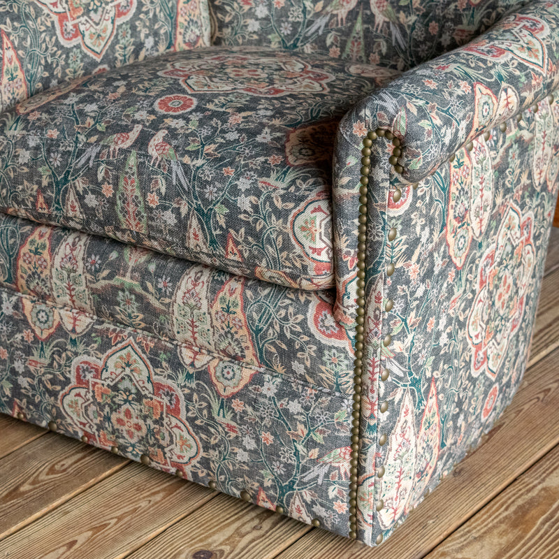 Arm close-up of a swivel chair upholstered in muted sage green fabric with bird and floral motifs