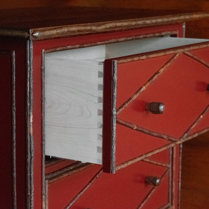 Close-up of the dovetail drawer of a tall, red painted four-drawer dresser with diamond details against a wooden wall