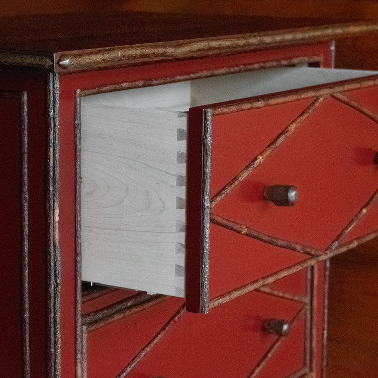 Close-up of the hickory foot of a tall, red painted four-drawer dresser with diamond details on a wooden floor