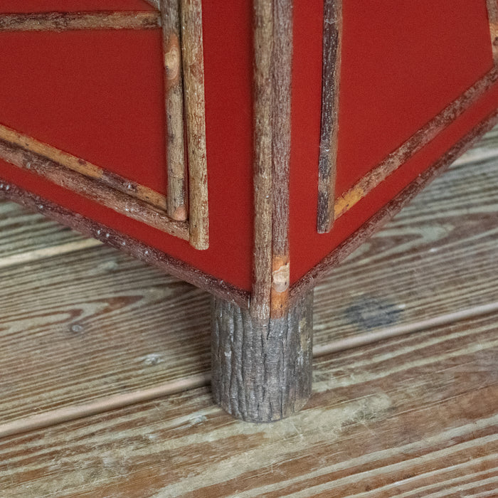 Close-up of the hickory foot of a tall, red painted four-drawer dresser with diamond details on a wooden floor